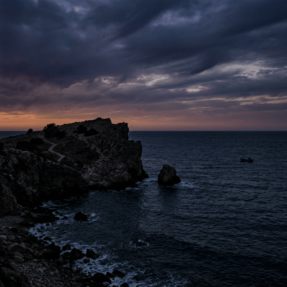 Rocky cliff jutting into dark ocean waters at twilight with overcast sky and small fishing boat